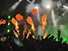Silhuetter av et konsertpublikum foran flammer, grønt lys og røyk på scenen.