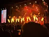 Konsertscene med flammer, rødt lys, artister og publikum i forgrunnen.