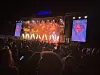 Publikum ser en konsert med lysende scene, artister og to store videoskjermer.