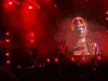 Rødt opplyst konsertscene med artist på storskjerm og publikum i forgrunnen.