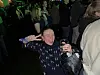 Smilende kvinne holder en drink blant mennesker i et mørkt, grønnbelyst selskapslokale.