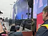 Publikum står foran en stor utendørsscene med lys, skjermer og vakter.