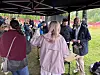 Mennesker samles under et telt ved et utendørs arrangement, med plen og fargerike gjerder i bakgrunnen.