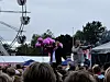 Publikum foran en utendørsscene med lilla ballonger og et pariserhjul i bakgrunnen.