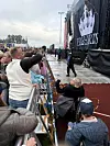 Publikum står ved en stor utendørsscene med lysrigg og svart sceneteppe.
