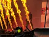 En scene med kraftige flammer i bakgrunnen, en mørk silhuett og teknisk utstyr i forgrunnen.