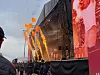 Publikum ser mot en stor scene med røde skjermer og flammer fra pyroteknikk.