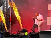 Vokalist synger på en scene med røyk, scenelys og høye flammer på hver side.