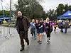 En mann går foran en gruppe mennesker ved et utendørs arrangement med sperringer og telt.