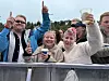 En smilende folkemengde bak en sperring, med flere som holder opp drikkebegre.