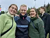 Fire smilende personer står tett sammen utendørs, iført varme klær.