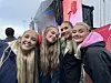 Fire unge kvinner smiler mot kameraet foran en utendørsscene med en videoskjerm.