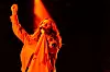 Artist med mikrofon og løftet arm i oransje scenelys mot mørk bakgrunn.