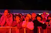 En tettpakket konsertpublikummengde står bak et metallgjerde i rødt og rosa lys.