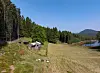 Et åpent jordbruksområde med små bygninger, skog, vann og fjell i bakgrunnen.