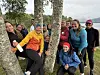 En smilende treningsgruppe står samlet rundt bjørketrær utendørs.