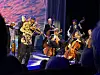 Et strykeensemble spiller på en scene med fiolinister og cellister i fargerikt scenelys.