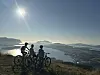 Tre syklister står med terrengsykler på en høyde med utsikt over fjord og fjell.