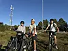 Tre personer med terrengsykler står i et åpent landskap under blå himmel.