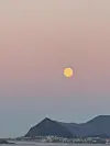 En gyllen måne henger på en rosa-blå himmel over fjell og en kystby.