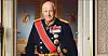 Eldre mann i mørk militæruniform med medaljer og blått bånd i et utsmykket rom.
