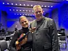 En ung fiolinist og en mann i mørk dress står sammen i en blåbelyst konsertsal.