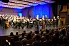 Orkester og kor opptrer på en opplyst scene foran et publikum.