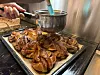 Et brett med nystekte kanelsnurrer står foran en bolle mens en hånd arbeider med baksten.