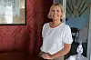 Kvinne i hvit bluse står i en historisk stue med mønstret tapet, maleri og eldre interiør.