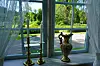 Ornamentert vase og to lysestaker står i en vinduskarm med utsikt til en grønn hage.