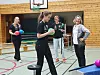 Fire personer står i en gymsal med fargerike baller og basketballkurv.