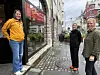 Tre kvinner står i en brosteinslagt bygate utenfor en butikk.