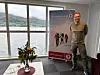 En mann står ved et DNT Sunnmøre-banner i et kontor med utsikt over fjord og fjell.