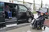 Rullestolbruker ved siden av en åpen bil med utfelt rampe i regnvær.