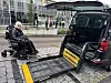Rullestolbruker ved en bil med utfelt rampe på et fortau.