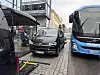 Blå bybuss kjører tett forbi parkerte biler i en smal, brosteinsbelagt gate.