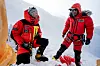 To klatrere i rødt utstyr står og kneler i et snødekt fjellandskap.