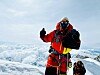 Fjellklatrer i rødt og svart utstyr står i snøen foran et vidstrakt islagt fjellandskap.