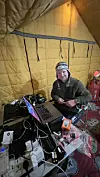 Person sitter i et telt omgitt av laptop, kamera- og annet elektronisk utstyr.