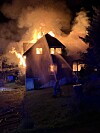 Et bolighus står i brann med flammer og tett røyk mot nattehimmelen.
