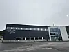 Moderne mørkt næringsbygg med glassinngang og parkeringsplass i overskyet vær.