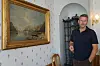 En mann står i et historisk interiør ved siden av et innrammet landskapsmaleri.