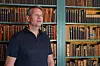 En mann står foran bokhyller med gamle bøker i et bibliotek.