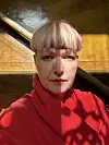Portrett av en person i rød genser foran et varmt belyst interiør.