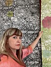 En kvinne i rosa skjorte viser fram et stort blomsterpreget kunstverk.
