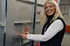 En smilende kvinne betjener en metallkonstruksjon i et industrielt innemiljø.