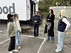 Fem kvinner snakker sammen på en parkeringsplass utenfor en bygning.