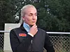 Ung kvinne i svart sportsjakke står utendørs foran et gjerde og ser mot siden.