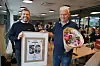 To menn står innendørs med en blomsterbukett og en innrammet markering med tallet 50.