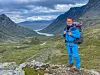 En mann i blått turutstyr står med sekk i et steinete fjellandskap under en skydekket himmel.